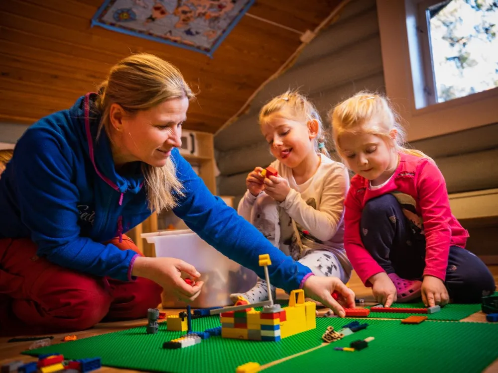 En person og to barn som leker med lego.
